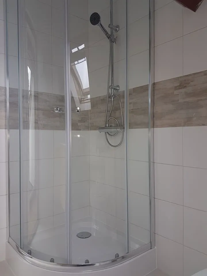 De ronde douchecabine met schuifdeuren, met de decoratieve band die op dezelfde hoogte doorloopt in het tegelwerk.