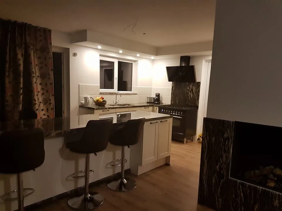 Dezelfde ruimte in de avond; rechts loopt hetzelfde donkere natuursteen door als omlijsting van de haard.