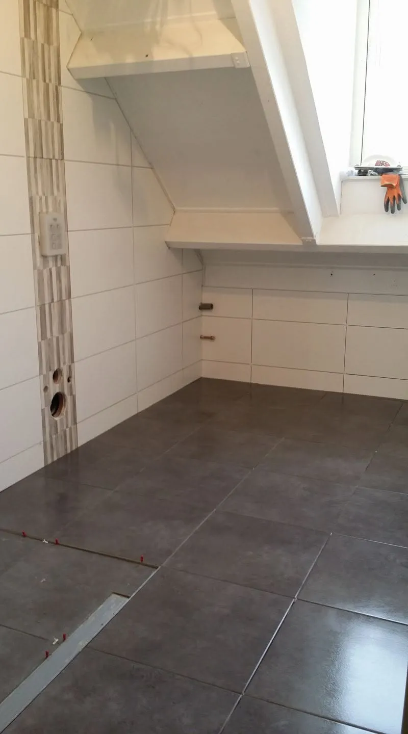 De nieuwe vloertegels liggen met tegelkruisjes op hun plek; in de wand zitten de doorvoeren al klaar.