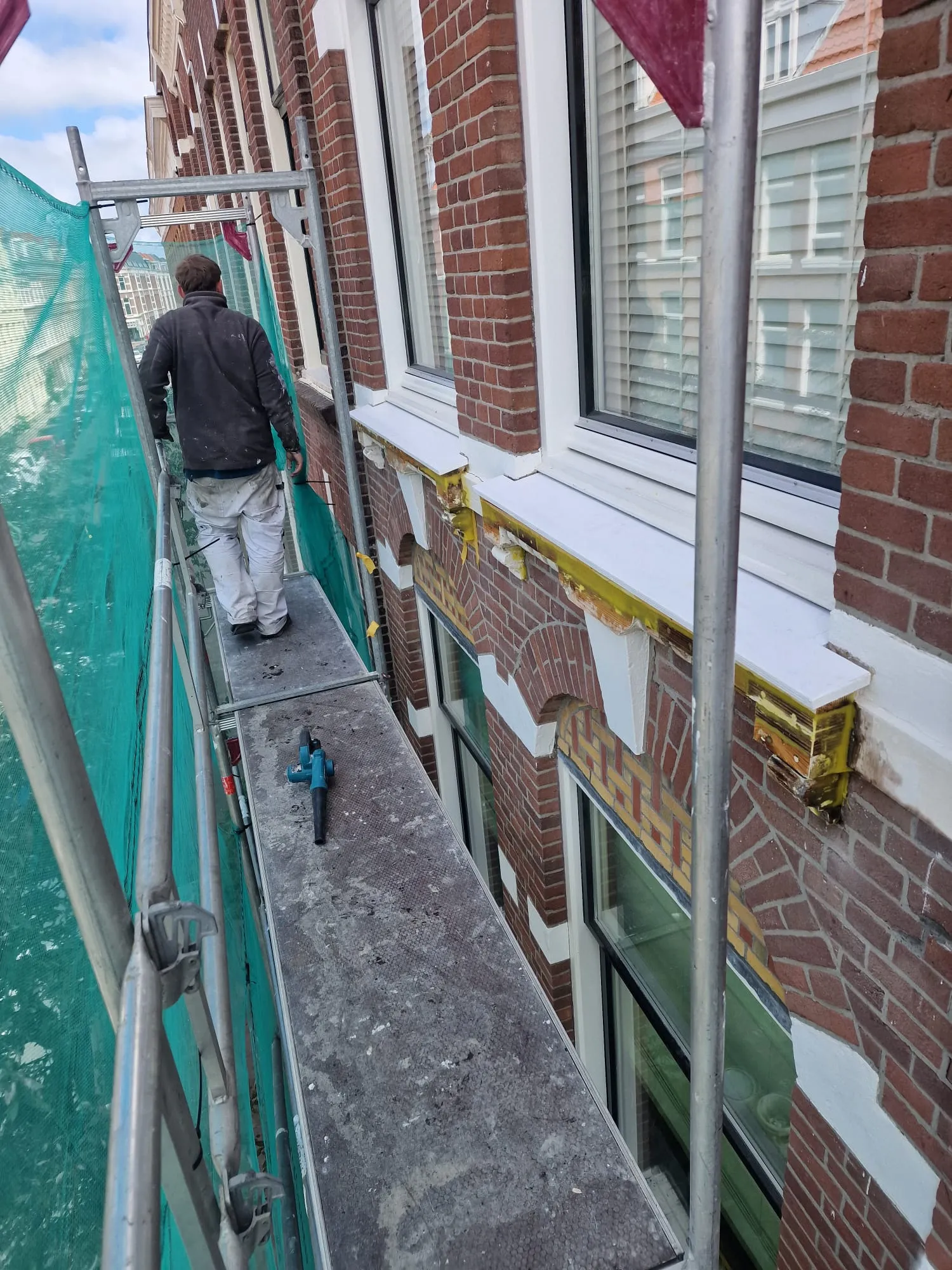 Werken vanaf de steiger langs de gevel; de lijsten zijn afgeplakt en de eerste waterslagen zijn al wit afgewerkt.