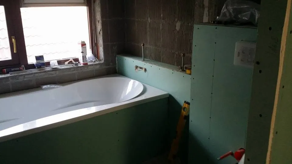 Het bad staat ingebouwd tegen de kaal gehakte muur; de omranding en de wanden zijn opgebouwd in groene plaat, klaar om te betegelen.