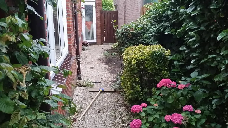 De zijtuin voor aanvang: een smalle strook grind tussen het huis en de heg, zonder verharding of beplanting.
